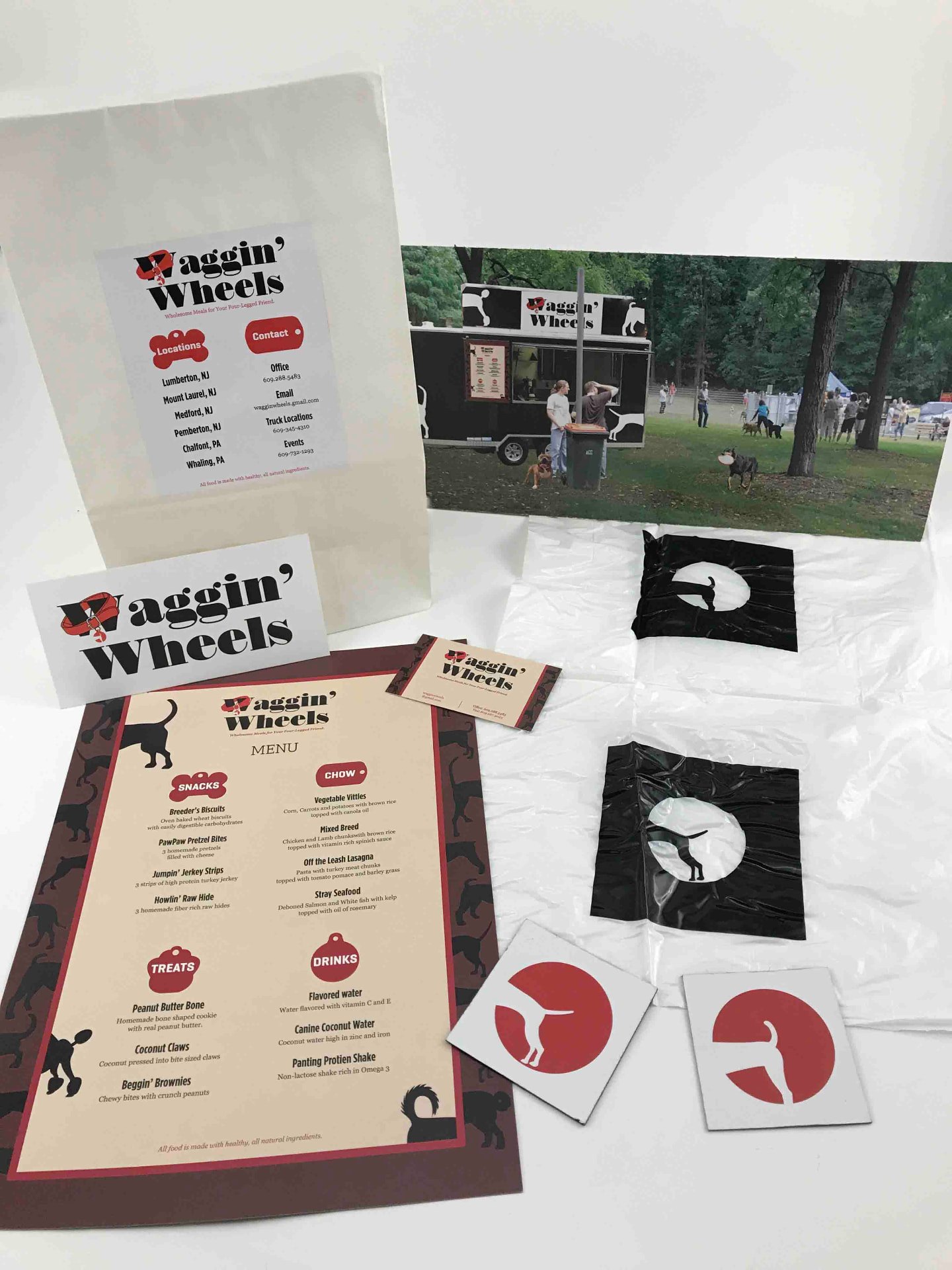 Waggin' Wheels brand pieces laid out together: takeout bag, logo card, menu, business card, printed bags, magnets and a print of the truck at a dog park