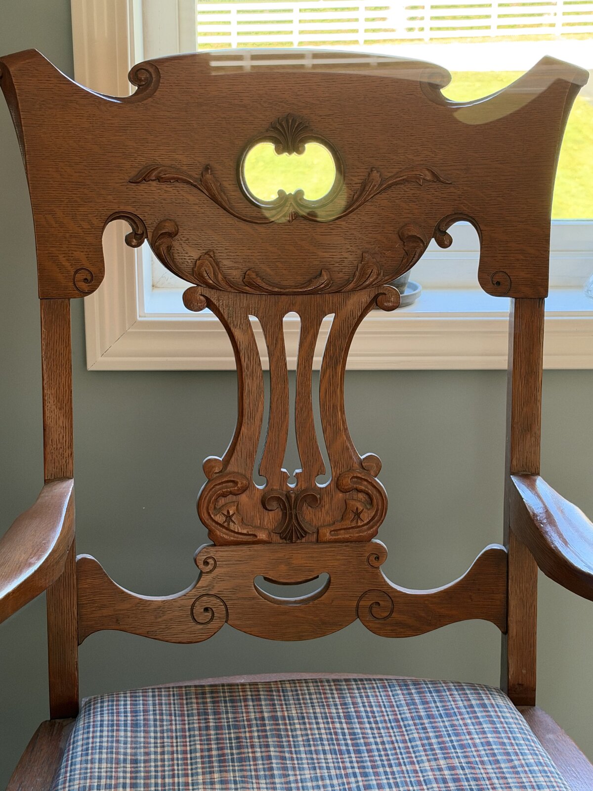 Carved back of the wooden armchair: a scrolled crest rail with a pierced opening above a lyre-shaped splat