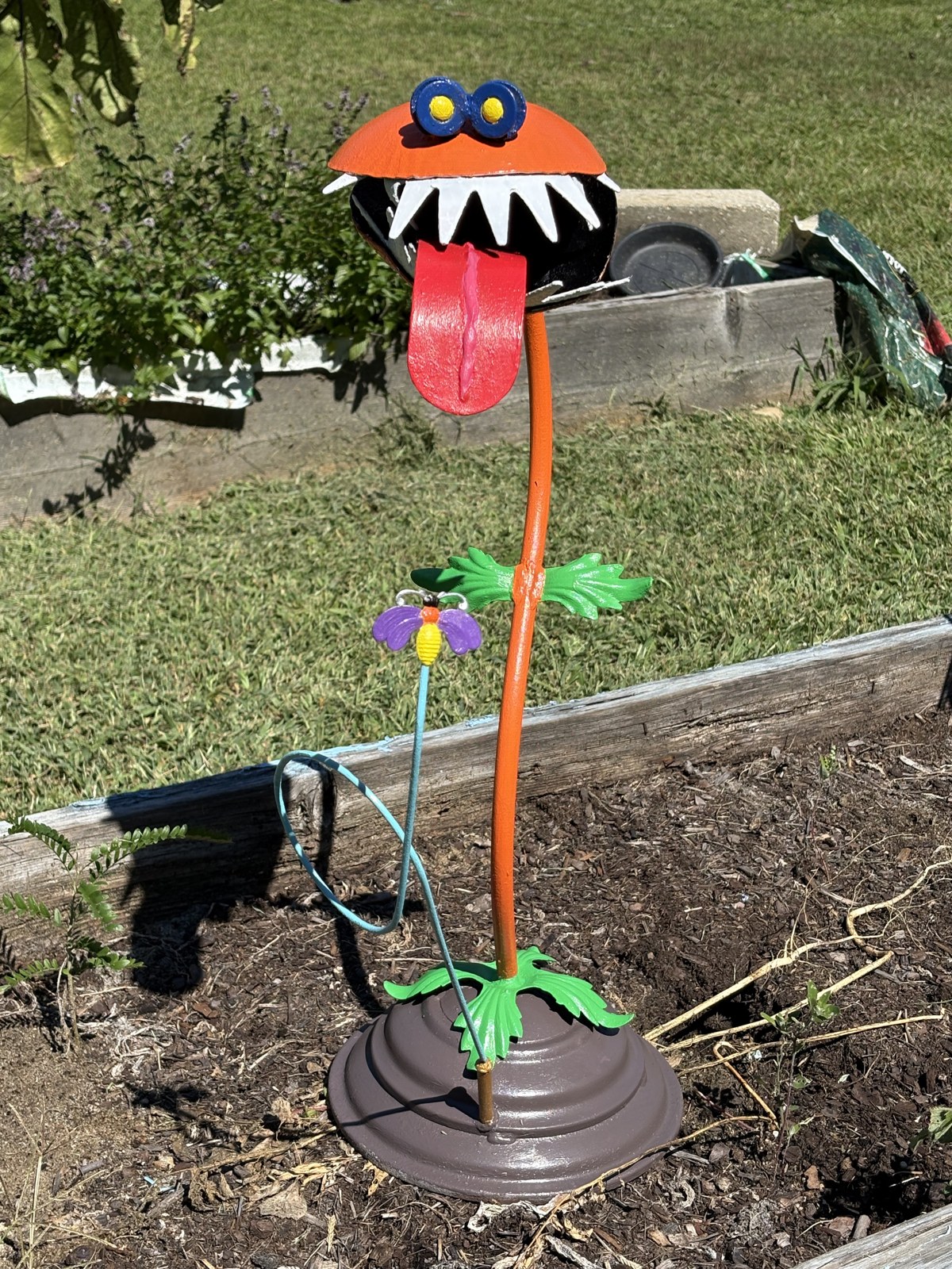 After: the garden sculpture painted with an orange head, red tongue, blue eyes, green leaves and a purple flower